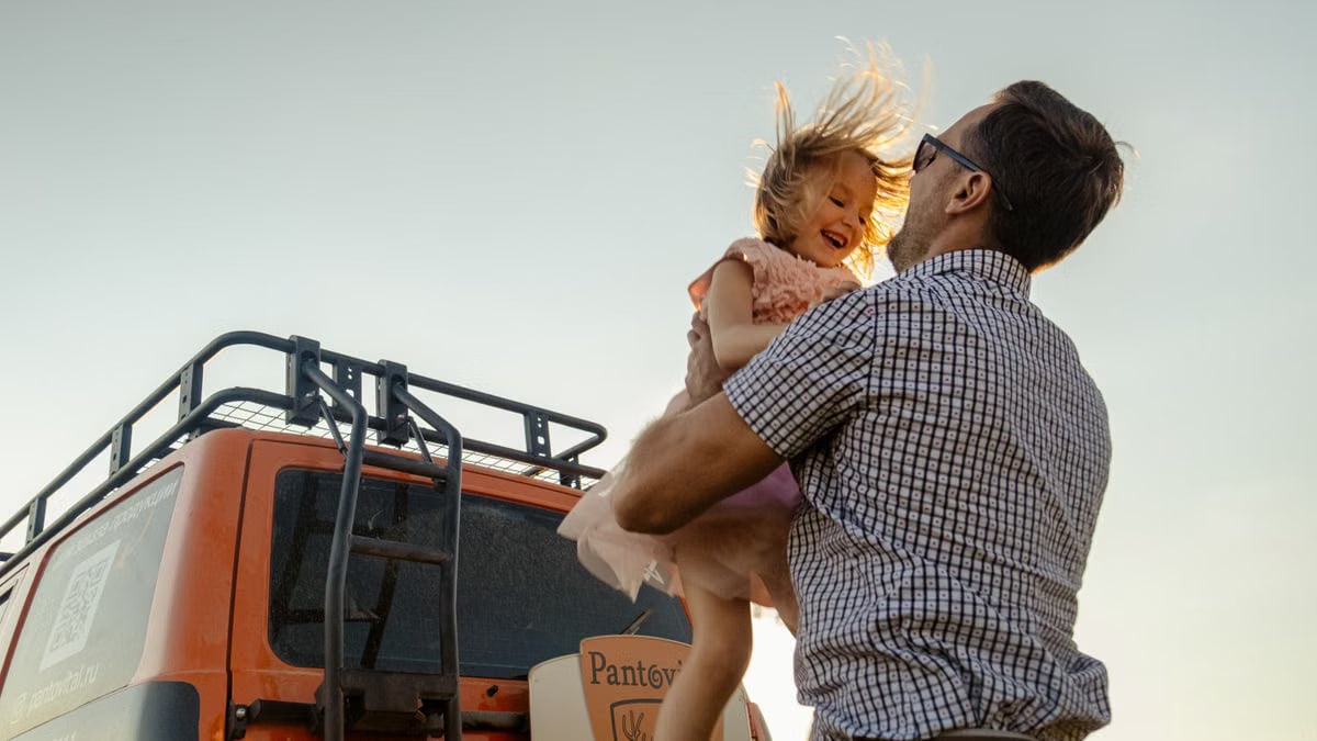 A joyful moment between a father and daughter outdoors with a van in the background.
